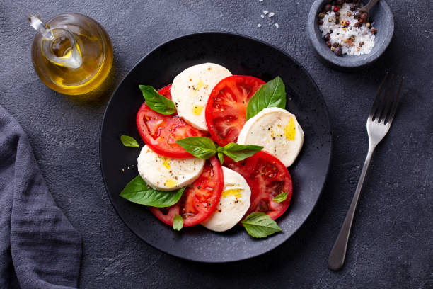istock Caprese salad with tomatoes, mozzarella cheese, basil. Dark background. Close up. Top view. 1265963091