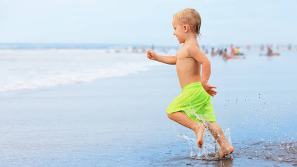 istock Child run with splashes by water pool along sea surf 1265964501