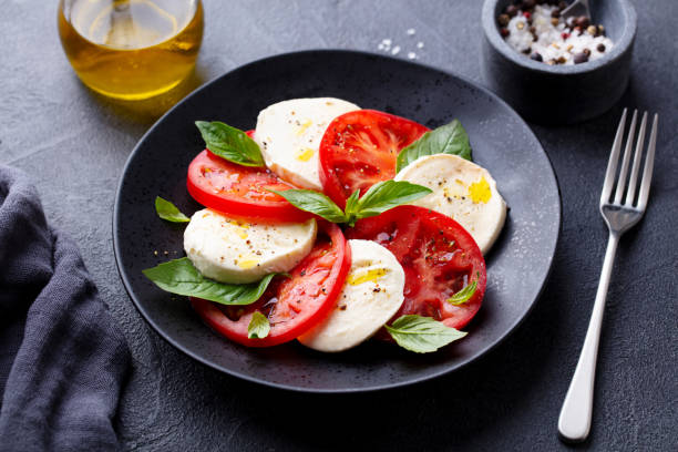 caprese salad with tomatoes, mozzarella cheese, basil. dark background. close up. - basil bowl cooked cheese imagens e fotografias de stock