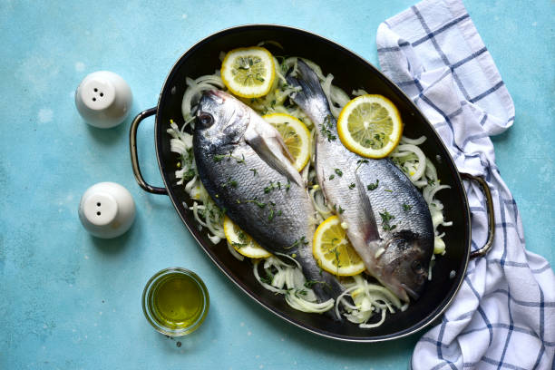 Raw fresh dorado prepared for baking with onion, lemon and thyme in a skillet pan. Top view with copy space.