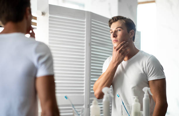 istock Handsome young man looking in the mirror, touching his chin 1265964923