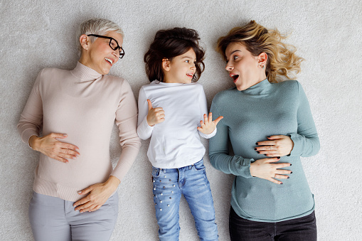 Female members of multi generational family are lying on the carpet.