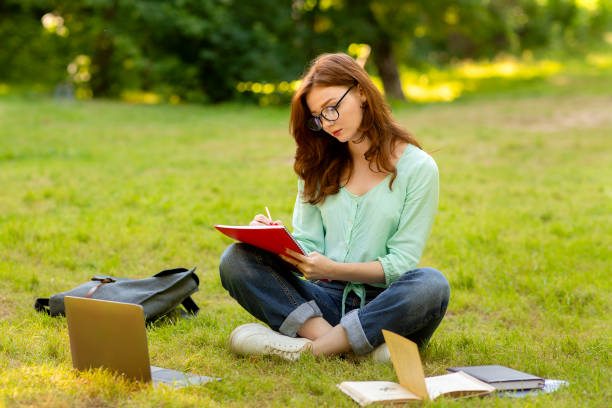 istock Beautiful redhead student girl preparing for exams in park, writing notes 1265970894