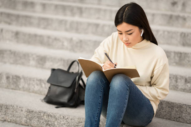girl writing in diary, sitting on the gray stairs - filipino ethnicity audio imagens e fotografias de stock