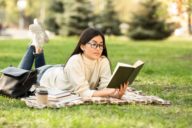 Girl reading a novel lying on the grass Preparing For Exams. Focused asian teen girl reading book lying on blanket in park hot filipina women stock pictures, royalty-free photos & images