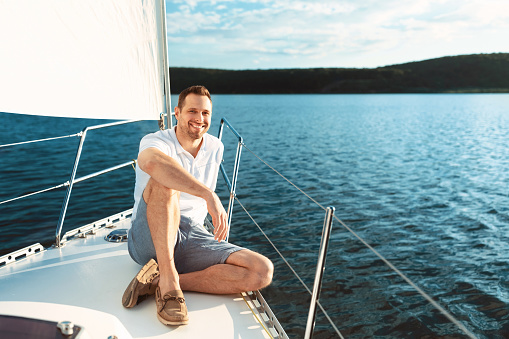 Yacht Ride. Joyful Man Sitting On Boat Deck Sailing Across The Sea, Smiling To Camera Enjoying Sea Trip. Empty Space