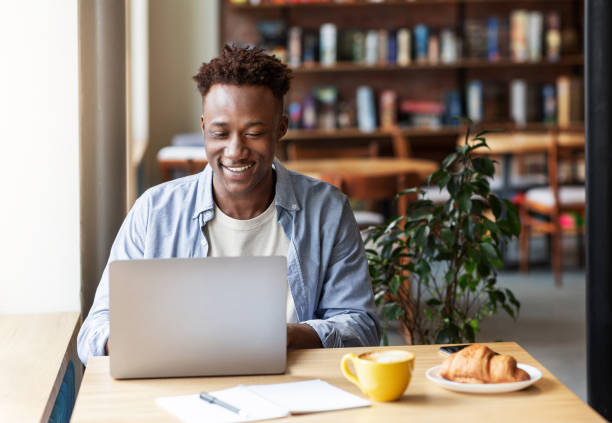 istock Happy black guy working online on laptop computer at cozy city cafe, free space 1265972394