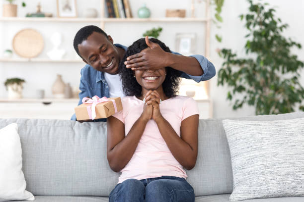 homem africano com caixa de presente cobrindo seus olhos de mulher - birthday present family facial expression birthday - fotografias e filmes do acervo