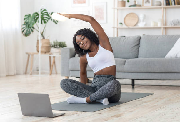 istock Sporty black girl exercising at home, using laptop 1265989275