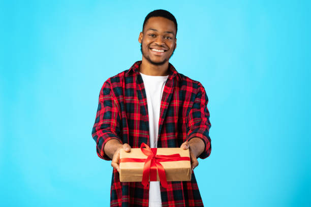 istock Cheerful African Guy Giving Gift To Camera Posing In Studio 1265989675