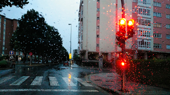 Driving in rainy weather, stop sign, red traffic light in empty avenue. Crossroad in the foreground. Raindrops on the windshield . Lugo city, Galicia, spain.