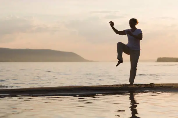 Woman praticing tai chi chuan at sunset on the beach. Chinese management skill Qi's energy. solo outdoor activities. Social Distancing