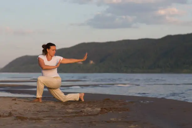 Photo of Woman praticing tai chi chuan at sunset on the beach. Chinese management skill Qi's energy. solo outdoor activities. Social Distancing