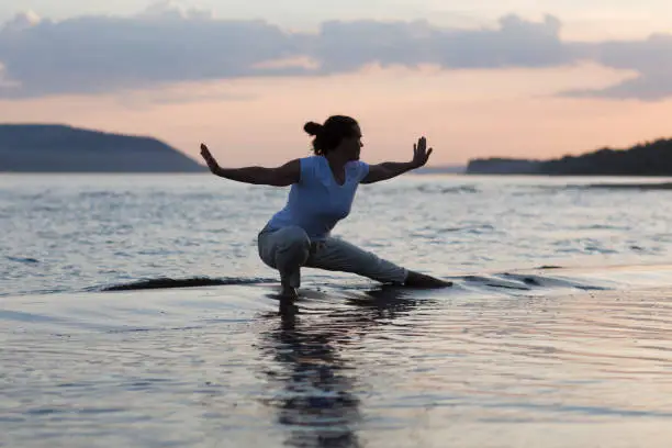 Photo of Woman praticing tai chi chuan at sunset on the beach. Chinese management skill Qi's energy. solo outdoor activities. Social Distancing