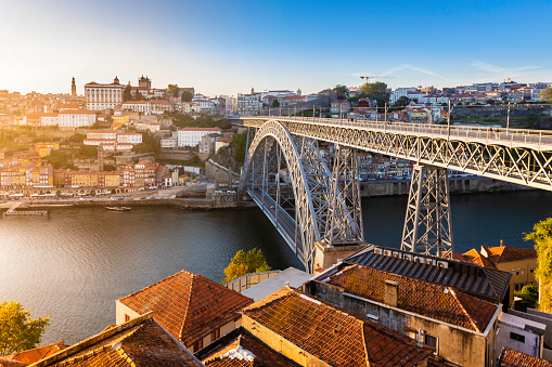 The Ribeira or riverside in Porto with Luís I Bridge seen accross the Douro river with restaurants and tourists along the riverbank at sunset, a popular tourist destination and one of UNESCO's World Heritage Sites.