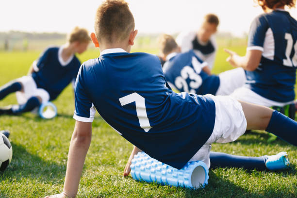 session d’étirement de soccer scolaire. jeunes footballeurs utilisant des rouleaux de mousse. muscles roulants d’enfants sur le terrain de football d’herbe - foot massage photos et images de collection