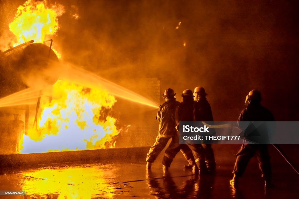 Firefighters extinguishing an industrial fire Firefighters practicing extinguishing an industrial fire at the fire station holding on to the hose spraying the fire at a storage tank. Firefighter Stock Photo