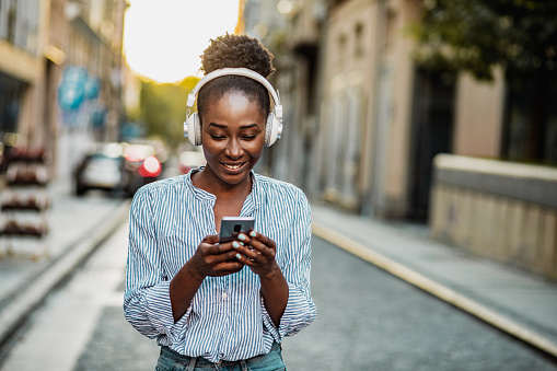 African American woman in the city, wearing headphones and using smart phone