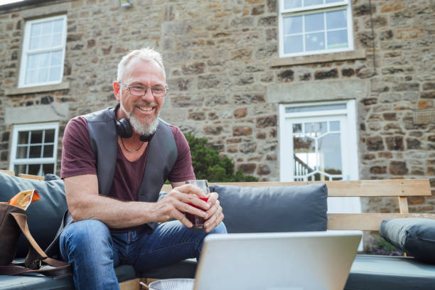 Freelance Work in the Outdoors A mature Caucasian man having a video call on a digital tablet while sitting outdoors on a bench with cushions. He is working from home during the Coronavirus pandemic. common beet audio stock pictures, royalty-free photos & images