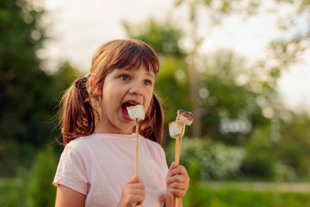 istock Little girl eats marshmallows toasted over a fire. 1266028805