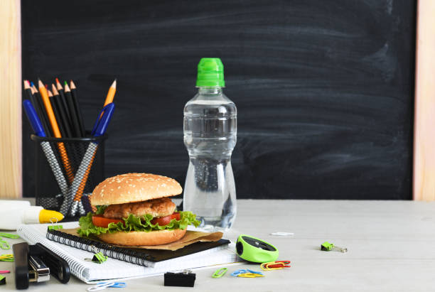 Back to school. Quarantine education. lunch box with hamburger, water and school accessories on the background of the school board. Back to school. Quarantine education. lunch box with hamburger, water and school accessories on the background of the school board. beef pad stock pictures, royalty-free photos & images