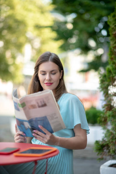 istock Charming brown-haired female reading sitting in cafe, reading newspaper 1266032041