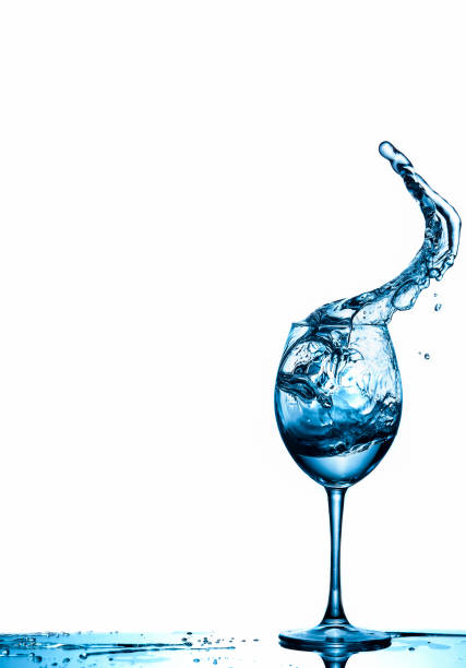 istock Clear Wineglass With Water Flows and Drops In Motion Against Pure White Background. Vertical image Composition 1266041277
