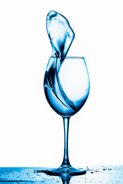 istock Clear Wineglass With Bluish Water Splash In Motion Against Pure White Background. Vertical image 1266041414