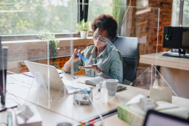 Close-up of a woman applying hand sanitizer before starting to work in office. Close-up of a woman applying hand sanitizer before starting to work in office. office cubicle mask stock pictures, royalty-free photos & images