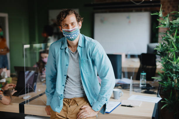 Portrait of businessman with face mask after returning back to work Portrait of businessman with cloth face mask after returning back to work. Young man wearing cloth face mask at work office cubicle mask stock pictures, royalty-free photos & images