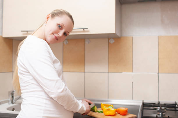 istock Positive Pregnant Female Cutting Vegetables on Chopping Board on Kitchen. Horizontal Image Orientation 1266048952