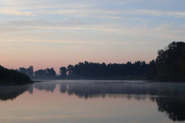 Beautiful calm sunrise dawn by the river with reflection on mirror water. Nice pastel nature landscape. Trees silhouette, fog, clouds and sunset photo.