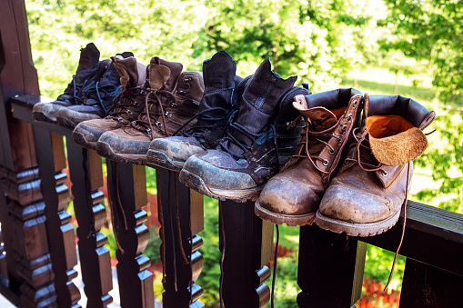 June 13, 2020 - Pieniny, Poland: Four pairs of dirty hiking shoes in a row on a balcony railing - muddy boots drying stacked in a row, close up.