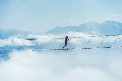 A person walks on a suspended rope bridge in the clouds.