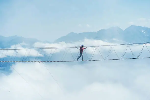 A person walks on a suspended rope bridge in the clouds. Extreme attraction.