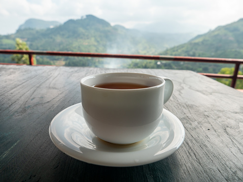 tea cup, black tea, herbal tea, blue cup, tea couple, tea ceremony, tea party, tea china, outdoor tea, cobalt blue, gold border on the cup, summer, spring, leisure, table, veranda, breakfast, coffee, coffee cup, blue tea cup on the back porch, blurred background with tree view green forest, countryside, cozy atmosphere suitable for relaxing on vacation