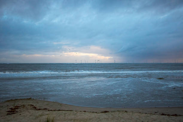 Distant offshore windfarm on the horizon. Coastal landscape scene. Shoreline of Great Britain. North sea off the East coast England with view of wind turbines from Caister UK.