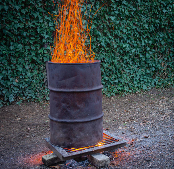 istock Life hack. Metal barrel with lid for burning branches in garden. Barrel on blurred background wall of ordinary ivy or ivy English. Selective focus. Ecology. Fire safety. 1266076806
