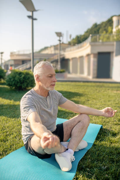 istock Grey-haired man sitting in lotus pose, meditating, hands in Gyan mudra 1266078856