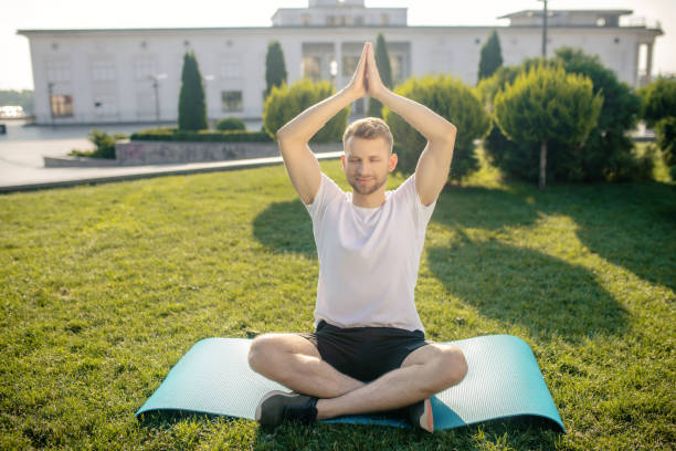 istock Young male practicing yoga outside, lifting his hands above head 1266078902