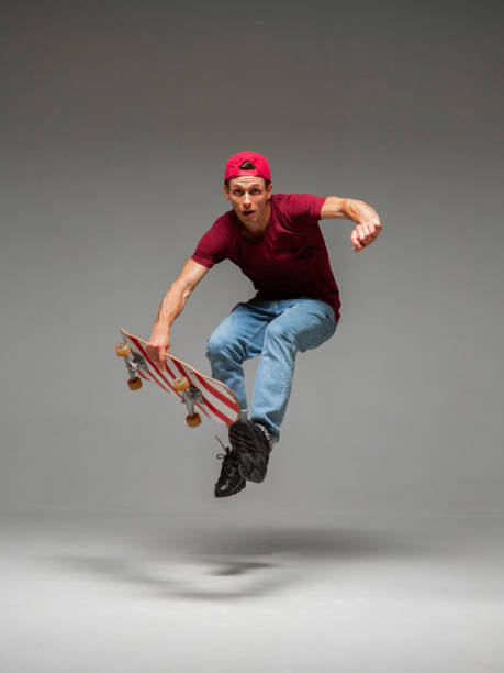 istock Cool young guy skateboarder jumps on skateboard in studio on grey background. Photography about skateboarding tricks 1266091590