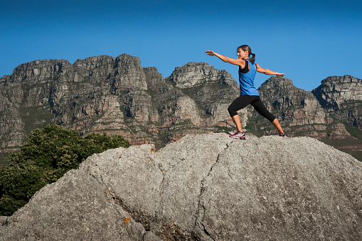 A woman strikes a yoga pose on top of a giant granite boulder  at Camp's Bay beach, Cape Town, South Africa