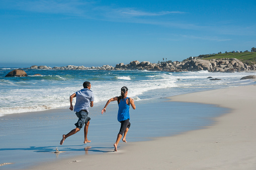 Mixed race male and Caucasian woman couple having fun and running competitively at Camp's Bay beach, Cape Town, South Africa