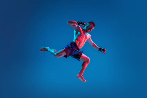 istock MMA. Professional fighter punching or boxing isolated on blue studio background in neon 1266096504