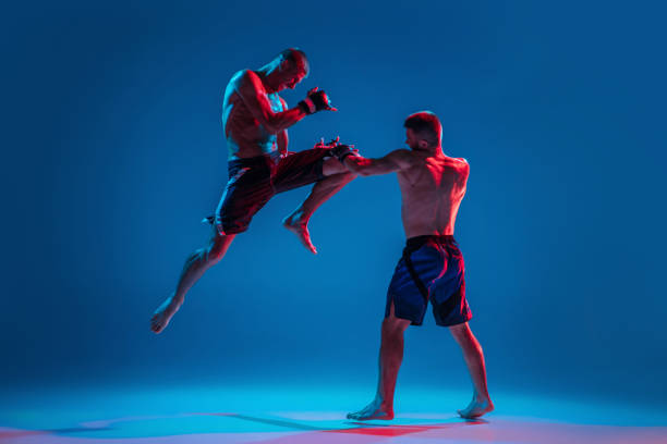 mma. dos luchadores profesionales golpeando o boxeando aislados sobre el fondo de estudio azul en neón - mixed martial arts combative sport boxing kicking fotografías e imágenes de stock