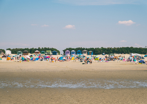 West Wittering, UK - August 11, 2020: A bright summer's day in the south of England, and this is the view looking up the beach of West Wittering in West Sussex towards a large number of sun-worshipping day-trippers.