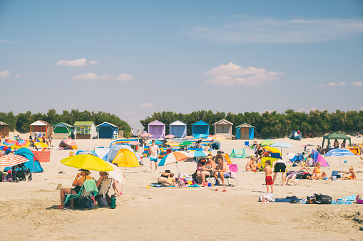 West Wittering, UK - August 11, 2020: A bright summer's day in the south of England, and this is the view looking up the beach of West Wittering in West Sussex towards a large number of sun-worshipping day-trippers.