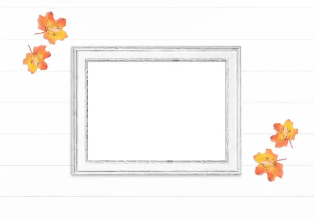 Empty white wooden frame with autumn leaves on white wooden background - wooden frame mockup for your design