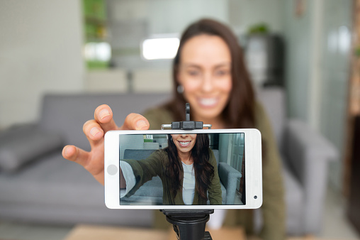 Feliz hembra vlogger grabando contenido en casa usando su teléfono celular photo