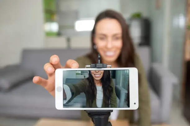 Photo of Happy female vlogger recording content at home using her cell phone